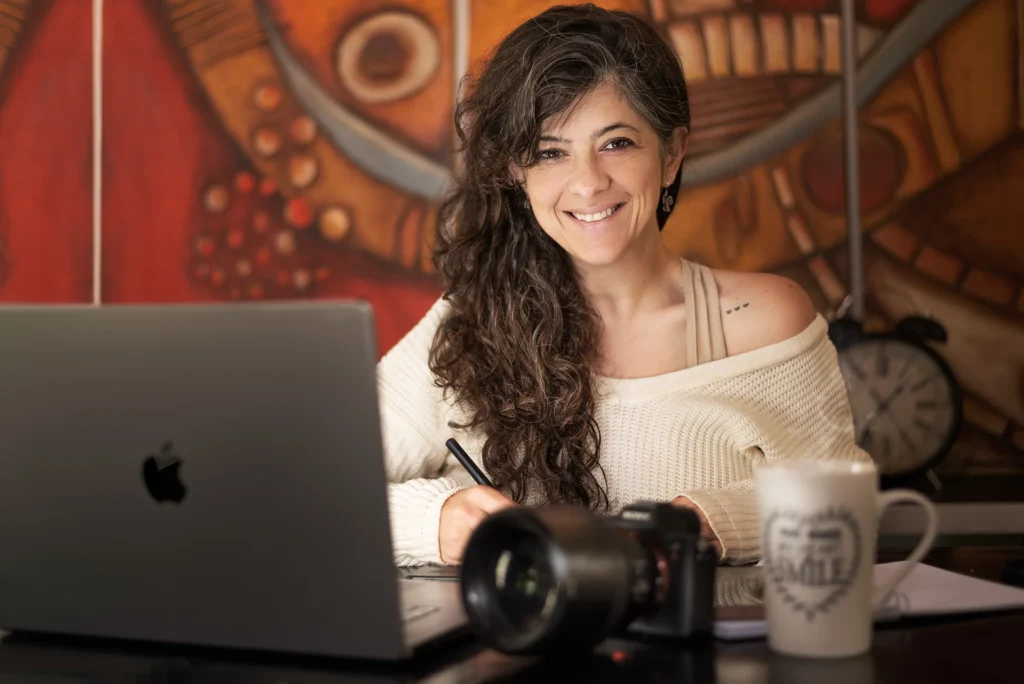 Ana editando fotos en su oficina, mirando a camara sonriendo.